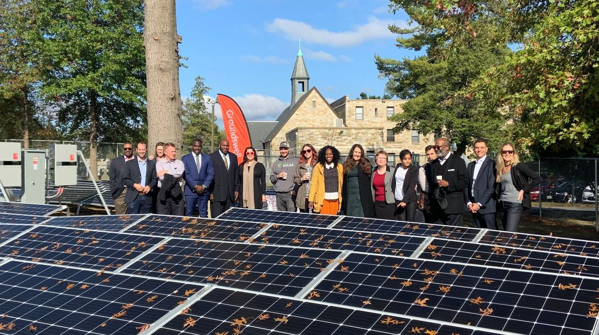 Group of people standing in front of House of Worship and behind array of solar panels